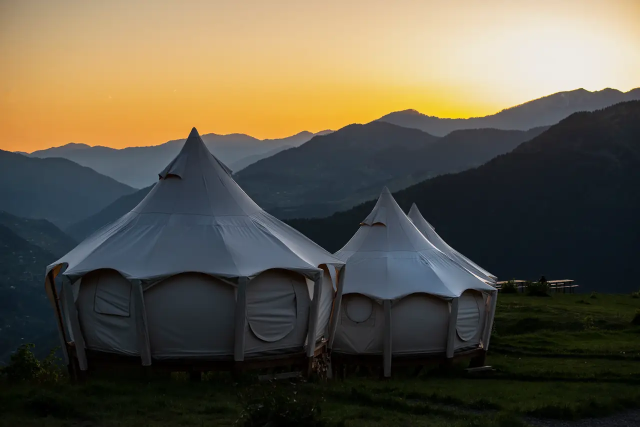 Two Lotus Belle tents in front of layered mountains under an orange sunset sky.