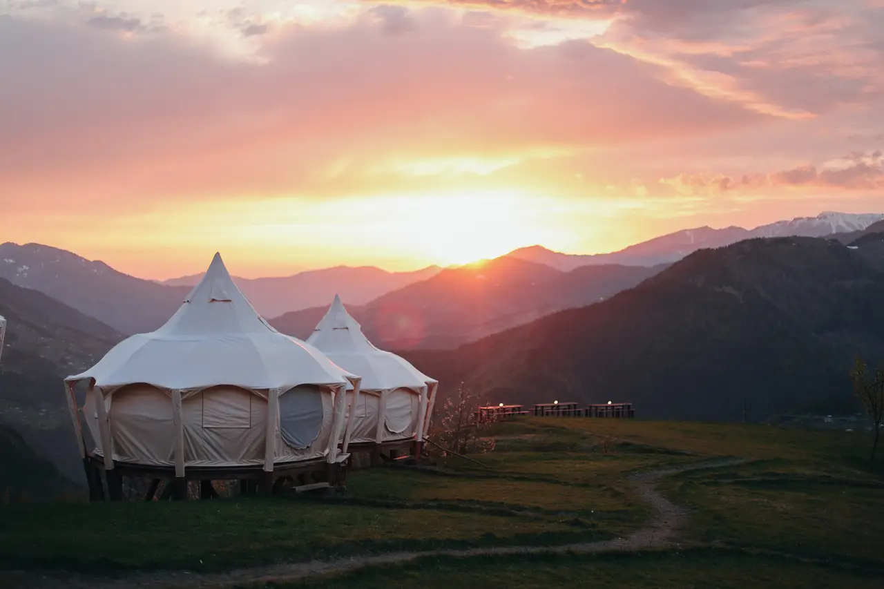 Two Lotus Belle tents on the meadow at sunset, with a pink and orange sky over the mountains and snow on the far peaks.